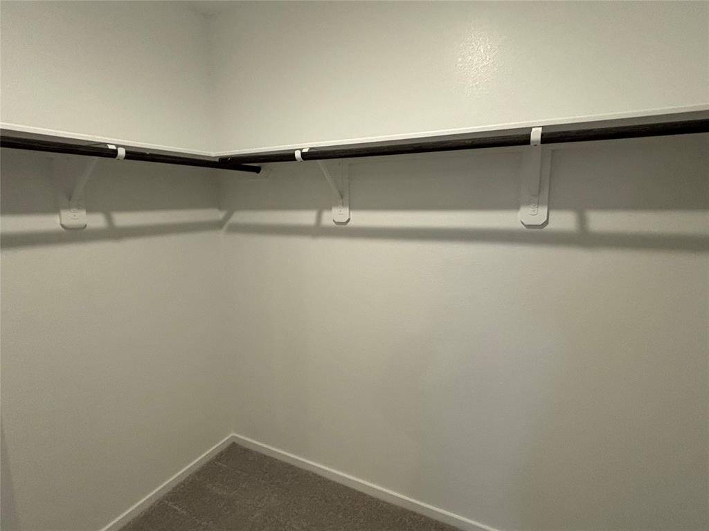 This photo shows a spacious walk-in closet with neutral walls, carpeted flooring, and multiple hanging rods for ample storage.