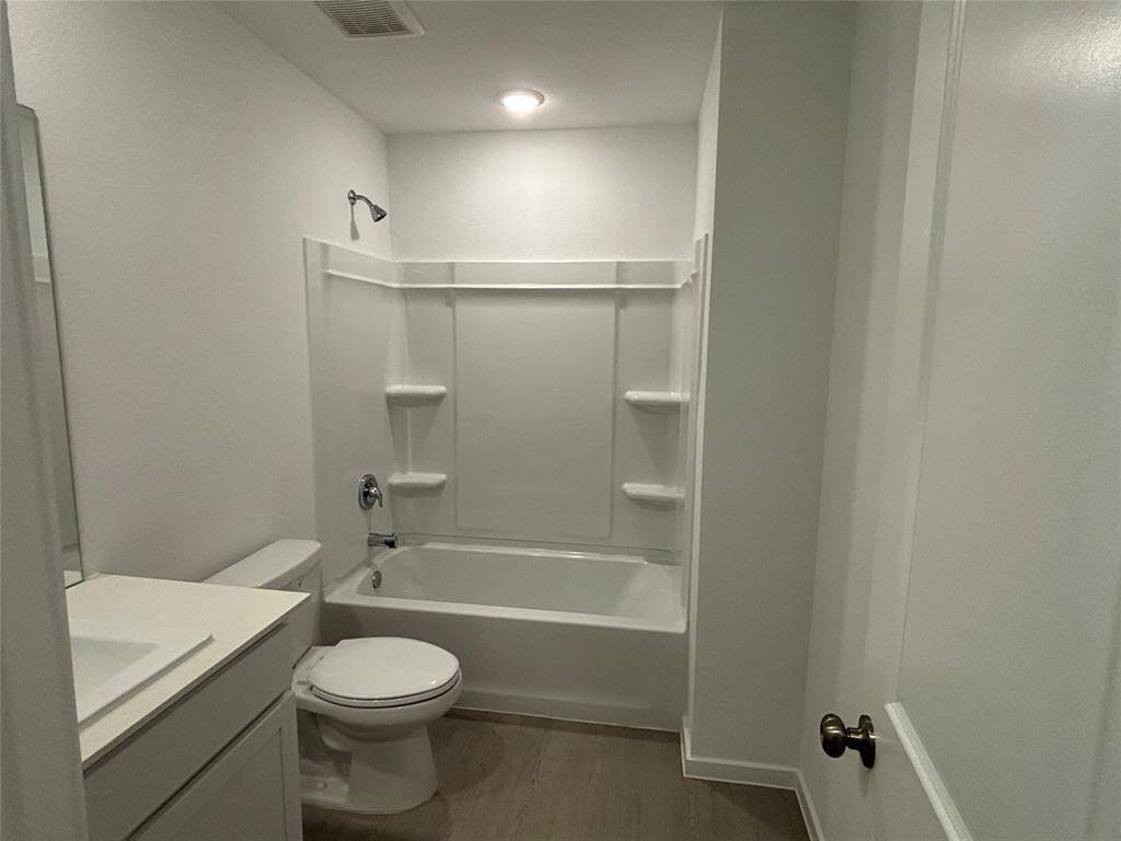 This bathroom features a clean, modern design with a white bathtub/shower combo, built-in shelving, a toilet, and a sleek vanity with a sink. The space is well-lit with recessed lighting and has a neutral color palette.