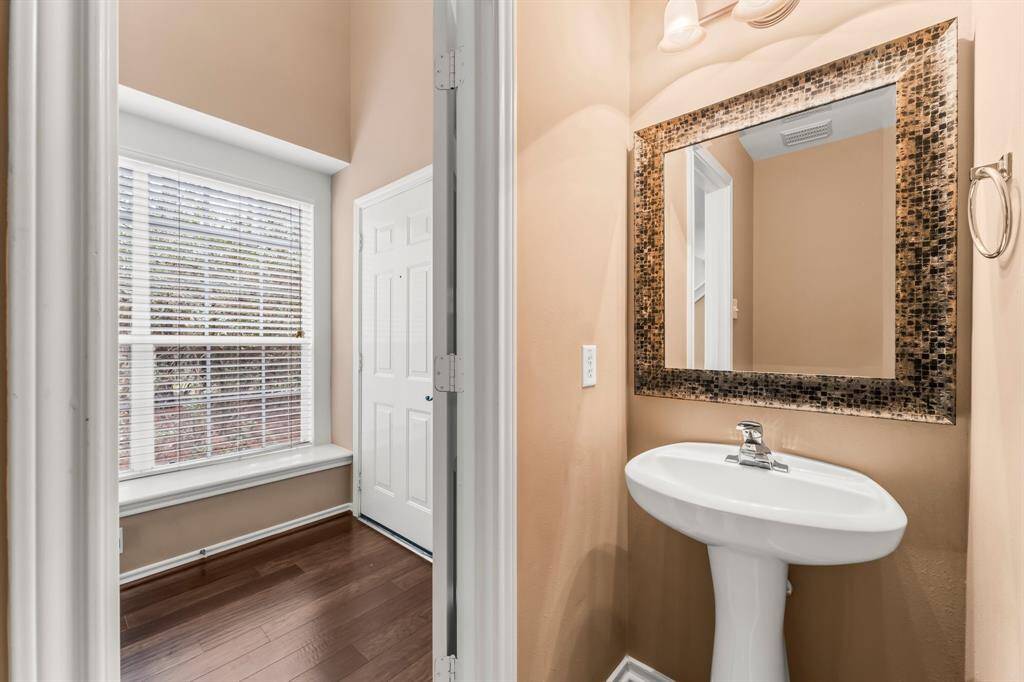 Half bath for guests  features tile flooring, pedestal sink,  toilet, and a framed mirror.