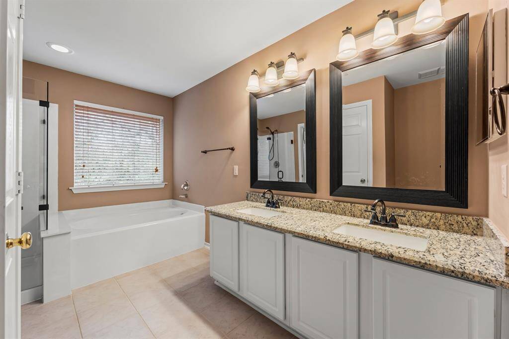 The double vanity area allows plenty of space when getting ready and is highlighted by framed mirrors, vanity lighting, granite countertop, and a medicine cabinet. A large window offers natural light while still providing privacy.