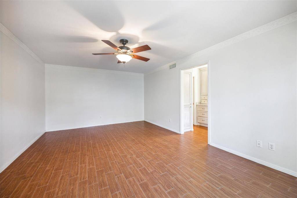 Primary bedroom with clean white walls, wood-look tile flooring, and a ceiling fan. Doorway leads to an adjacent bathroom.