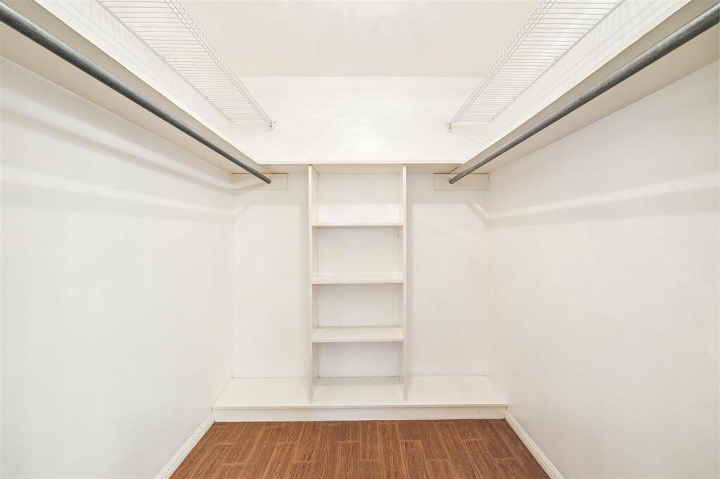 Large walk-in closet with wood-look tile flooring, ample hanging space on both sides, and built-in shelves for organized storage.