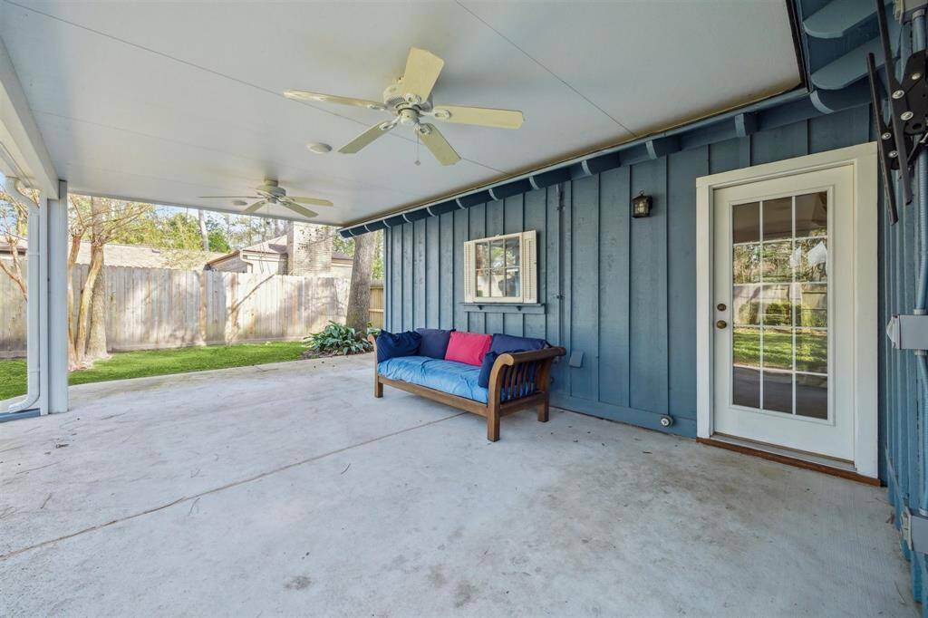 Covered patio with a comfortable outdoor sofa, ceiling fans, and a glass door leading inside. The area is ideal for relaxation and entertainment, overlooking a fenced backyard.