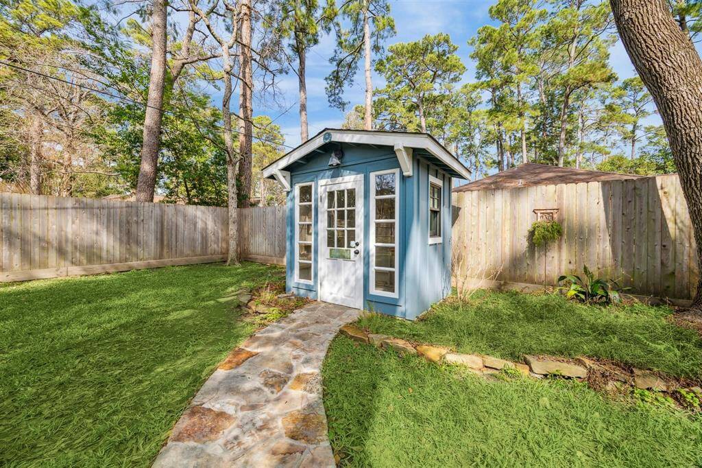 A quaint, blue garden shed is surrounded by lush greenery and trees, it features a stone pathway leading to the entrance, offering a charming and serene outdoor space.