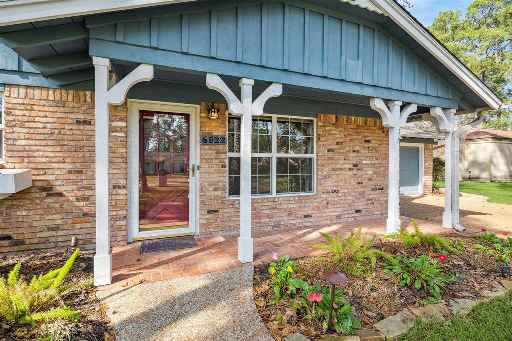 Charming brick home with a covered front porch, with white columns and decorative trim. The front door is accented by a large picture window, allowing natural light inside. Neat landscaping and a walkway enhance the curb appeal.