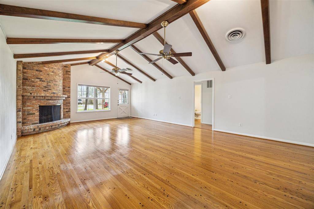 Family room has a vaulted ceiling with wooden beams, a brick gas log fireplace, and hardwood floors. Updated vinyl double-paned Large window and farmhouse door provide ample natural light.