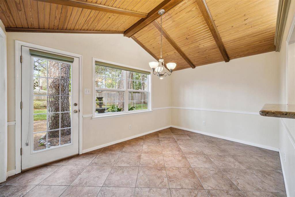 Dining room has a vaulted wood ceiling with exposed beams, large windows, and a glass door that opens to the backyard, providing ample natural light. The tiled floor and neutral walls create a warm, inviting space, ideal for a dining area or sunroom.