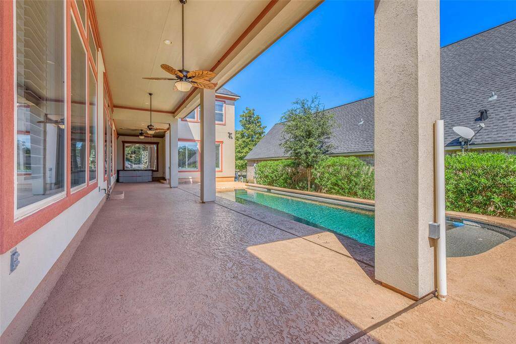 This photo showcases a spacious covered patio with ceiling fans, overlooking a private pool. The area is perfect for outdoor relaxation and entertainment, with a view of lush greenery and neighboring houses.