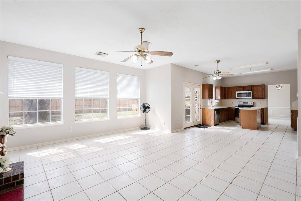 This bright, open-concept space features a large living area with tile flooring and abundant natural light from multiple windows. The kitchen is equipped with modern appliances, wooden cabinets, and a central island. Ceiling fans enhance comfort, and the layout flows seamlessly into the dining area, offering ample room for entertaining.