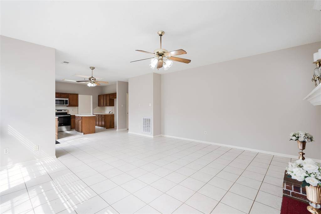 This photo showcases a bright, open-concept living area with tile flooring, neutral walls, and ceiling fans. It seamlessly connects to a modern kitchen featuring stainless steel appliances and wooden cabinetry, ideal for entertaining or family gatherings.