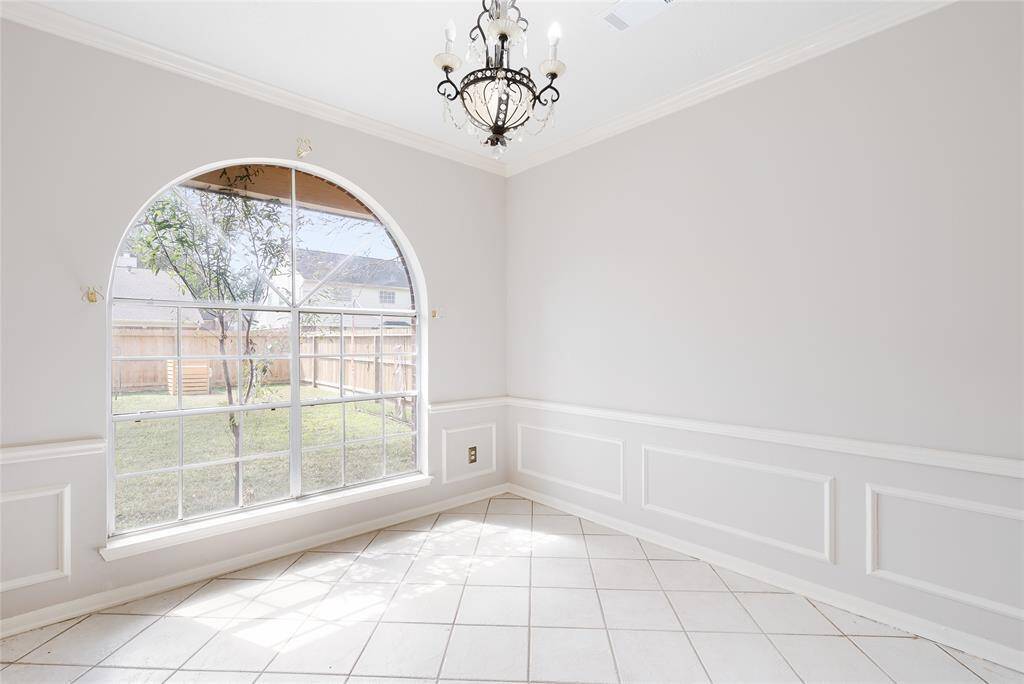Bright dining area with a large arched window, letting in plenty of natural light. Features elegant wainscoting, light-colored tiled flooring, and a decorative chandelier, creating a charming and inviting atmosphere.