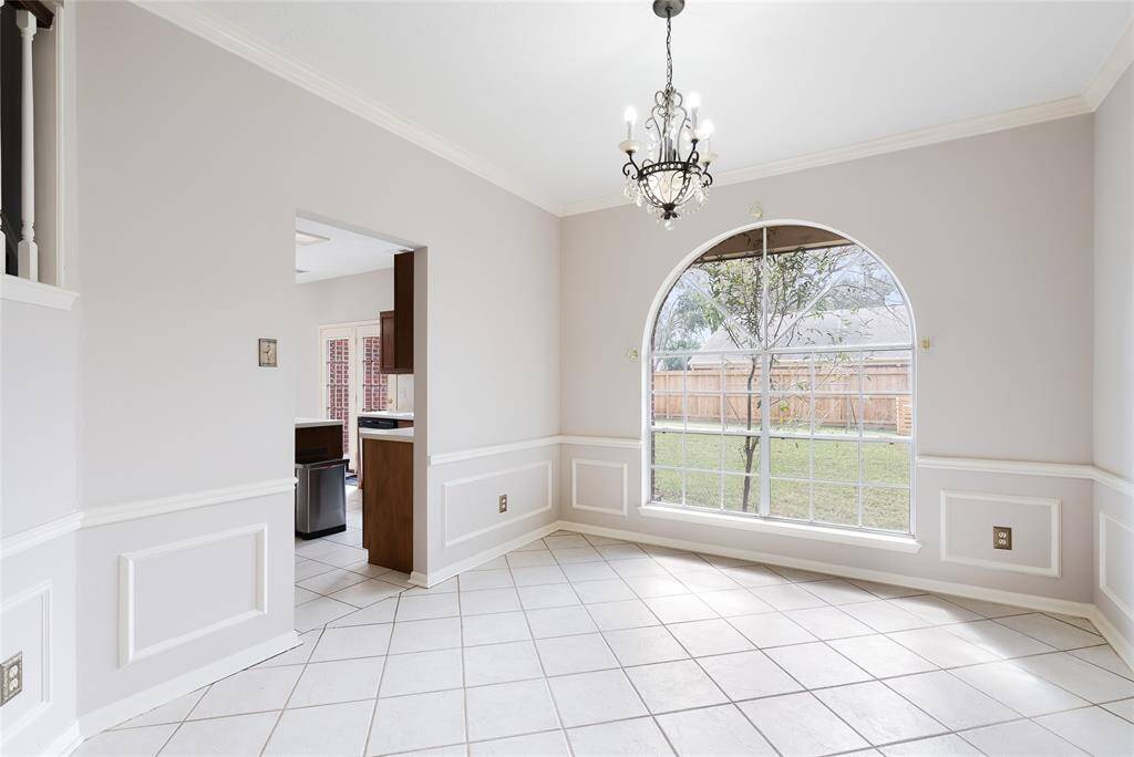 Bright dining area with large arched window, tile flooring, and elegant chandelier. Neutral walls with wainscoting add charm. Open access to the kitchen and view of the backyard.