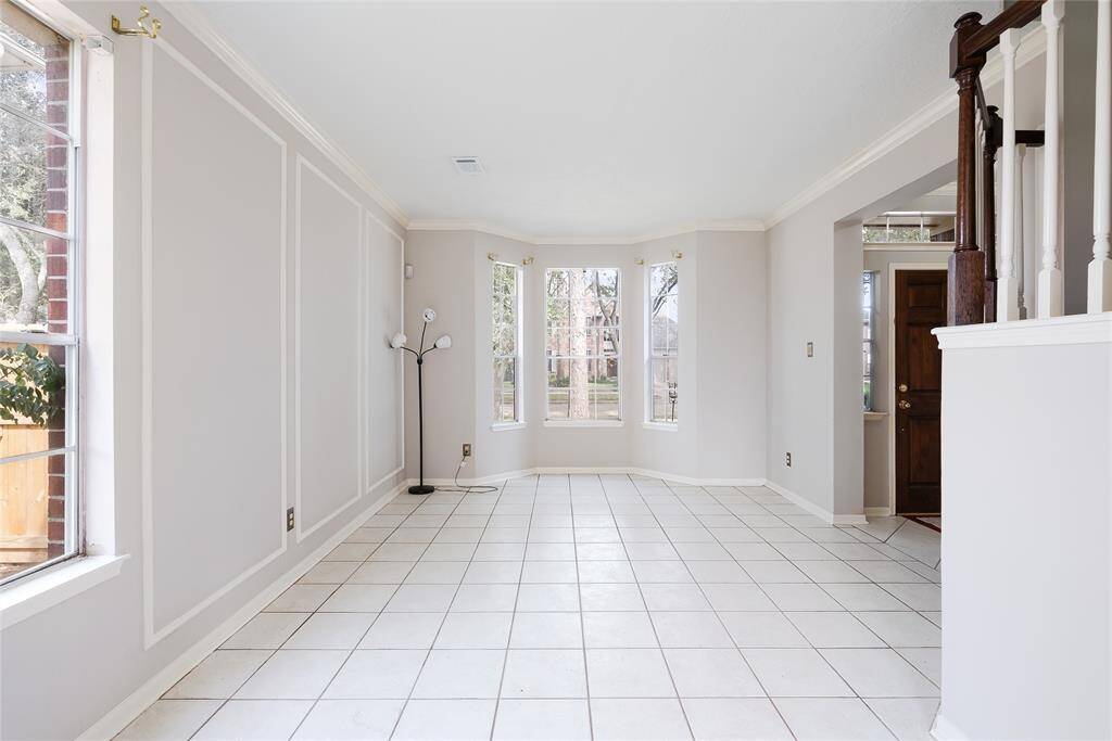 Bright and spacious room with large windows and white tiled flooring. Neutral walls with elegant molding create a clean, modern look. Perfect for a living or dining area with plenty of natural light.