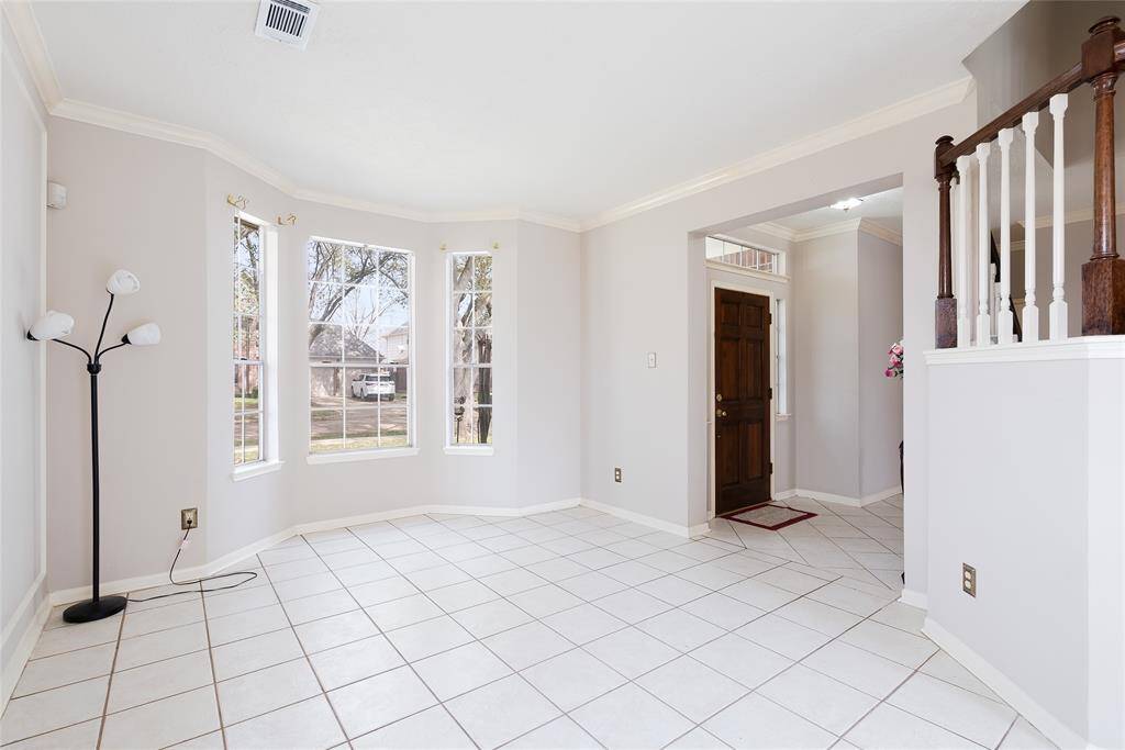 Bright, open entryway with large windows, neutral tiles, and a wooden front door. The space features a simple design with a floor lamp and partial wood railing, offering a welcoming atmosphere.