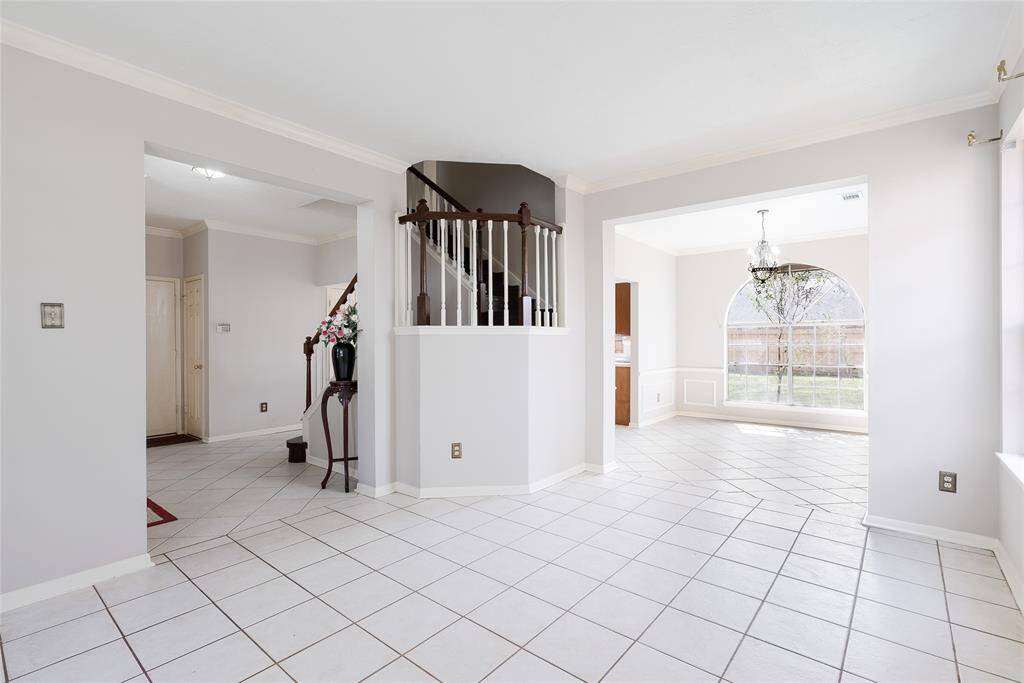 Bright, open living space with tiled floors, neutral walls, and a staircase leading upstairs. The area includes a large window in the dining space, offering plenty of natural light. Ideal for a welcoming and spacious home environment.