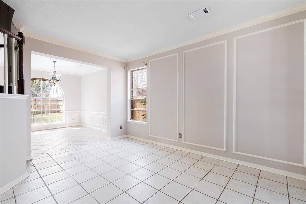 Bright and airy room with large windows, tiled flooring, and elegant wall paneling. Features an adjacent dining area with a chandelier, offering a view of the backyard. Perfect for comfortable living and entertaining.