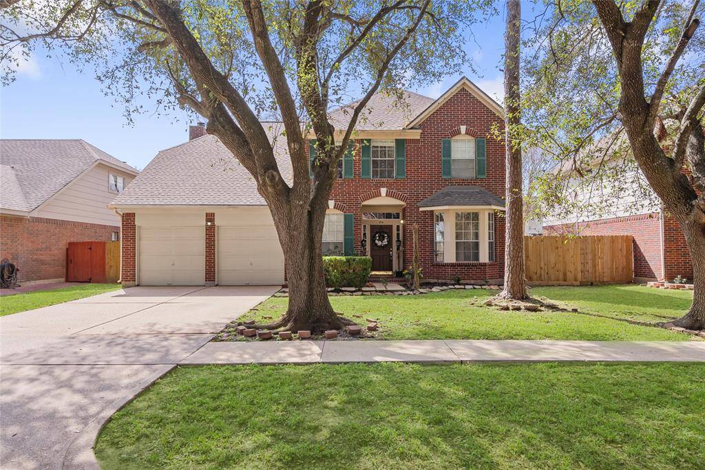 Charming two-story brick home with a well-maintained front yard and mature trees. Features include a two-car garage, inviting entryway, and attractive green shutters. Ideal for family living in a friendly neighborhood.