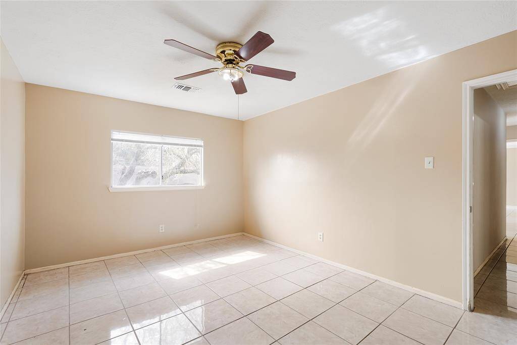 This room features neutral-colored walls, a ceiling fan, and tiled flooring. Natural light enters through a single window, creating a bright and airy atmosphere. Ideal for a bedroom or office space.