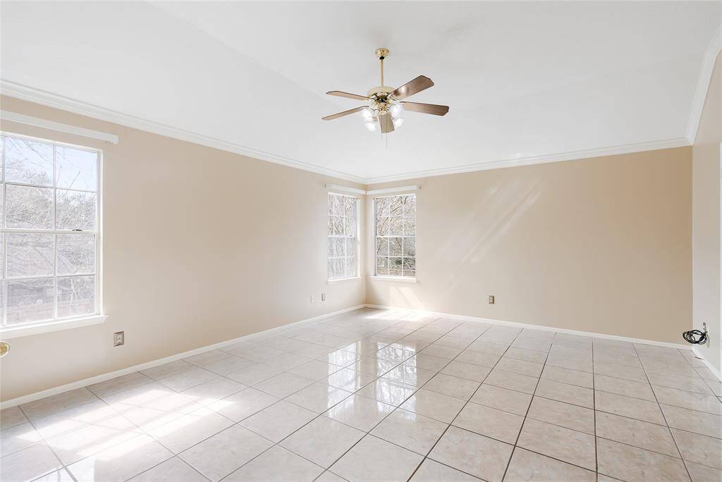 This spacious, bright room features large windows, neutral walls, and glossy tile flooring. A ceiling fan is centrally located, perfect for keeping the space comfortable. Ideal for a living area or a versatile family room.