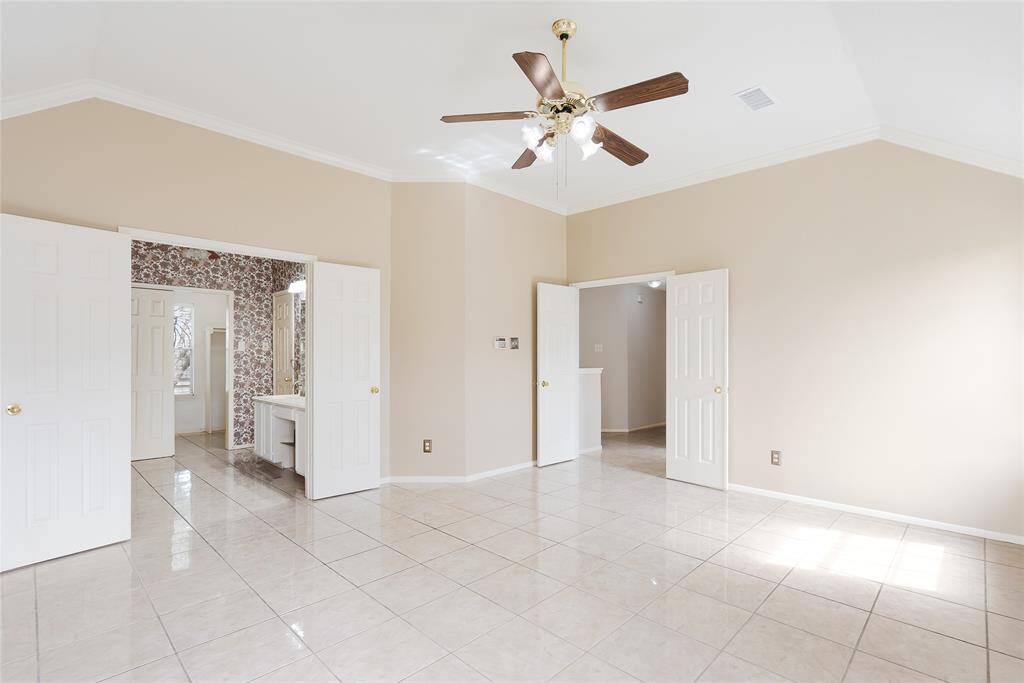 Spacious, bright room with glossy tiled flooring, neutral walls, and a ceiling fan. Features double doors leading to a patterned-wall bathroom with a large mirror and vanity. Ideal for a master bedroom setup.