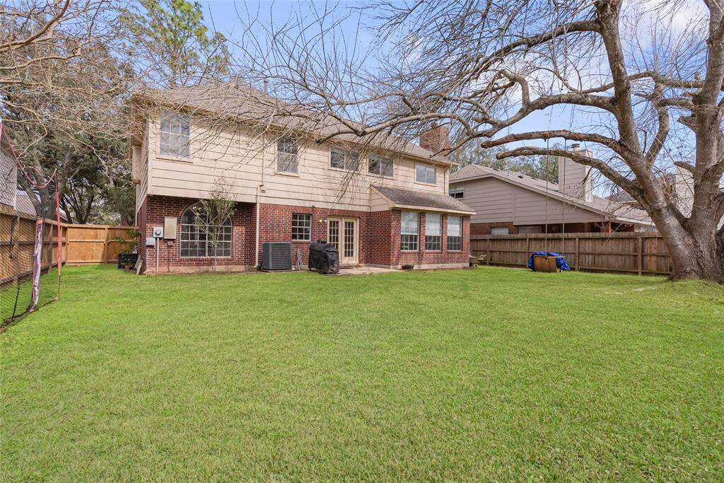 This photo shows a spacious backyard featuring a two-story house with a mix of brick and siding exterior. There's a large tree providing shade and a lush, well-maintained lawn. The yard is enclosed by a wooden fence, offering privacy and space for outdoor activities.