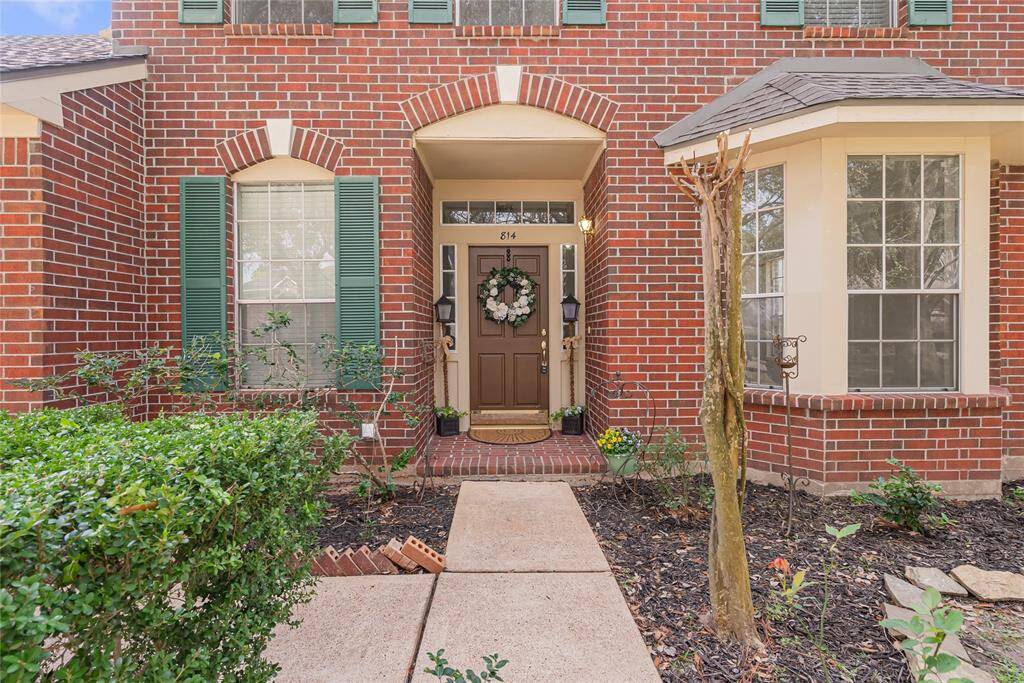 Charming two-story brick home with a well-maintained front yard and mature trees. Features include a two-car garage, inviting entryway, and attractive green shutters. Ideal for family living in a friendly neighborhood.