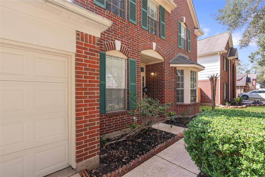 Charming two-story brick home with a well-maintained front yard and mature trees. Features include a two-car garage, inviting entryway, and attractive green shutters. Ideal for family living in a friendly neighborhood.