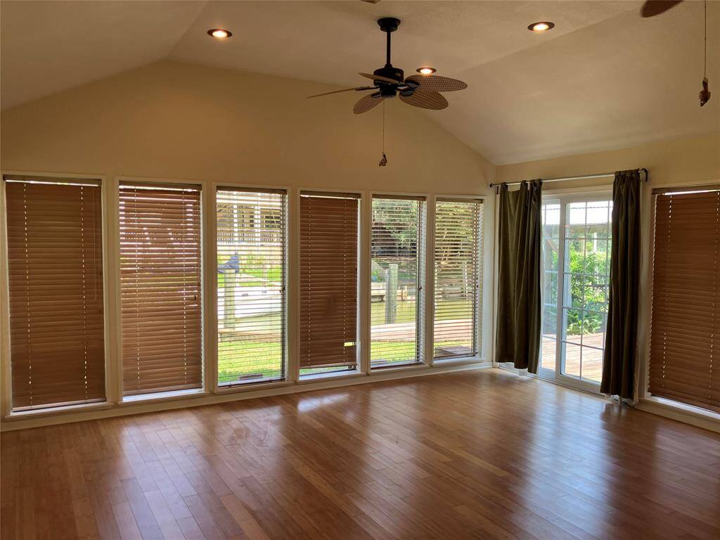 This room features a high ceiling with recessed lighting and a ceiling fan. It has large windows with wooden blinds, offering plenty of natural light and views of the outdoors. The hardwood floor adds a warm touch, and there's a sliding glass door leading to a patio area.