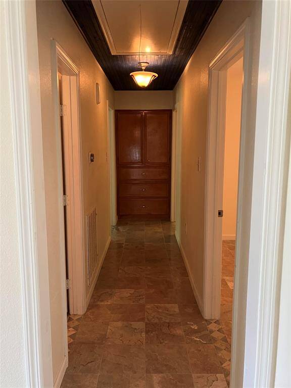 This hallway features tiled flooring and a wooden ceiling accent, with a built-in cabinet at the end. It offers access to multiple rooms on both sides, illuminated by a central light fixture.