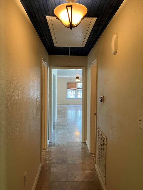 This photo shows a hallway with a light fixture and dark ceiling leading to a bright room with a window. The hallway has tiled flooring and doors on either side.