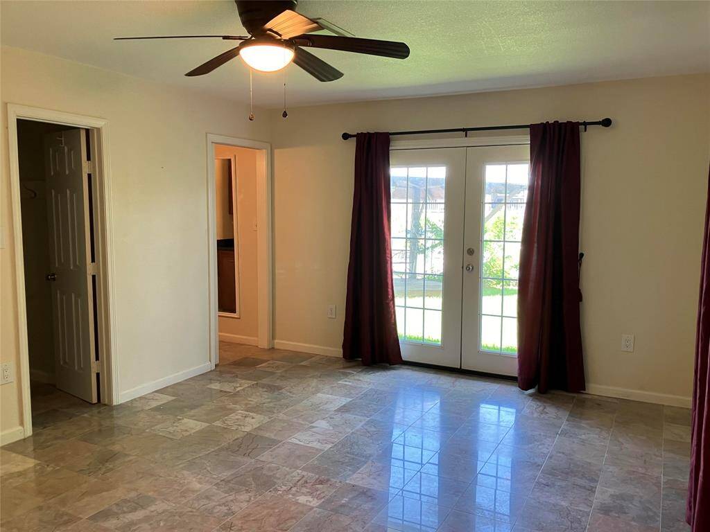 Bright room with tile flooring, ceiling fan, and large French doors leading to the backyard. Includes access to an adjacent hallway and closet.