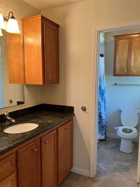This bathroom features a modern vanity with a dark countertop, wooden cabinets for storage, and a separate toilet area with additional cabinetry. The space is well-lit and has tiled flooring.