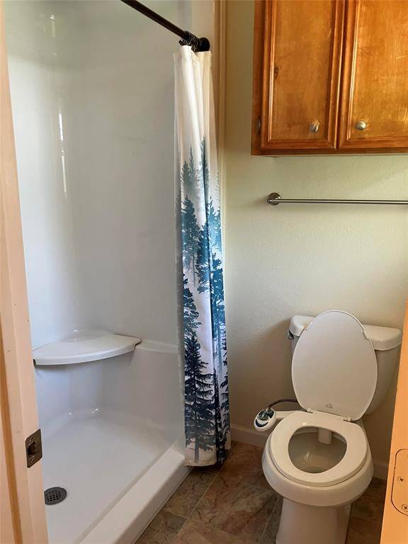 This bathroom features a shower with a forest-themed curtain, a toilet, and wooden cabinets for storage. The space is compact and practical.