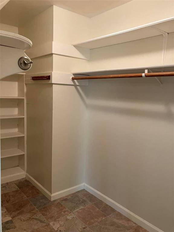This is a spacious walk-in closet featuring built-in shelves and a hanging rod, with neutral walls and tile flooring. Ideal for organized storage.