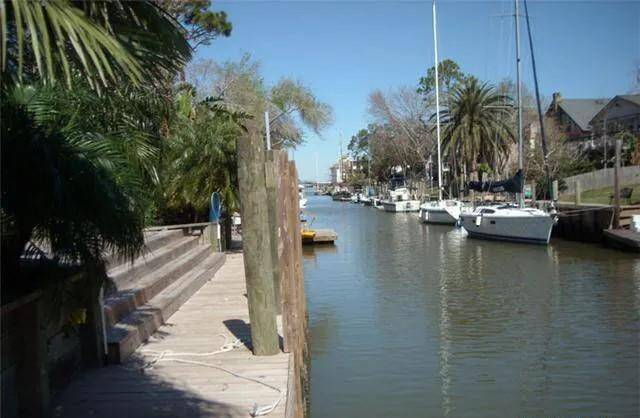 This photo showcases a serene canal lined with boats, offering a peaceful setting. The area features lush greenery and palm trees, suggesting a tropical or coastal vibe, ideal for a waterfront lifestyle.