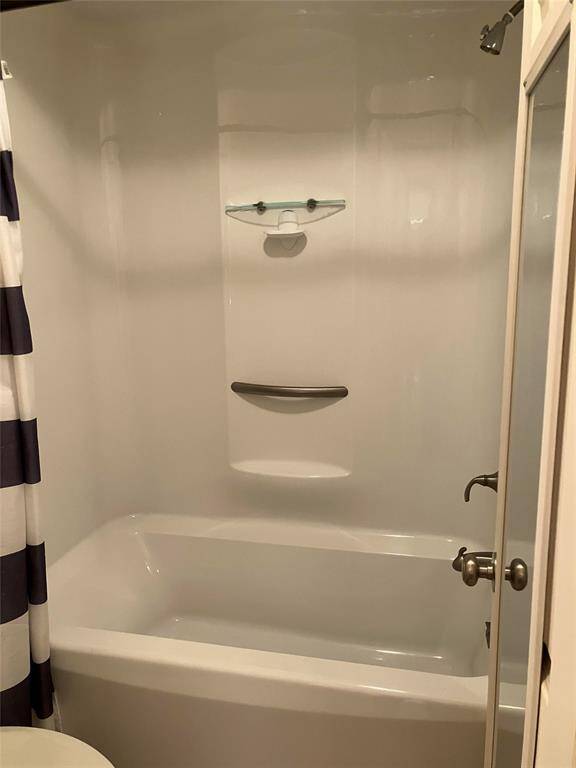 This photo shows a clean, modern bathroom with a white bathtub and shower combination. It features built-in shelving for storage and a neutral shower curtain. The fixtures are simple and functional, creating a cozy and practical space.