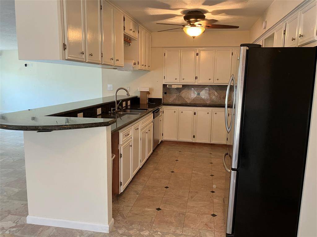 This kitchen features ample cabinetry and counter space with a sleek black countertop and tile backsplash. It includes modern appliances and a ceiling fan, offering a cozy and functional cooking area. The open layout connects to the living space, enhancing the home's flow and natural light.