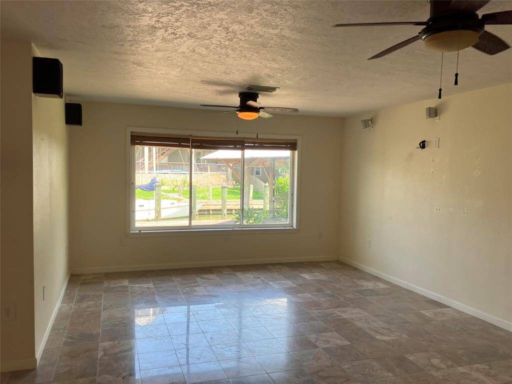 This room features tiled floors, neutral walls, a large window offering natural light and a view of the outdoors, and ceiling fans for comfort.