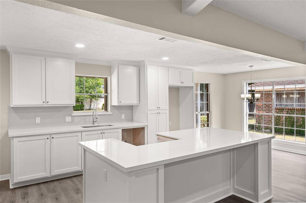 This spacious kitchen features large windows, high ceilings, white stained wood cabinets, quartz countertops, modern tile backsplash, recessed lighting, extended counter space, quartz kitchen island with space for breakfast bar, and a walk-in pantry all overlooking your huge family room.