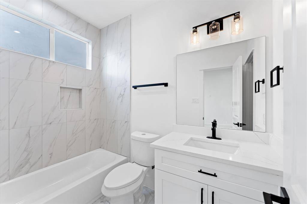 This photo shows a bright laundry room with white cabinetry, a utility sink, and hookups for a washer and dryer. The space has modern finishes and tiled flooring, creating a clean and functional area.