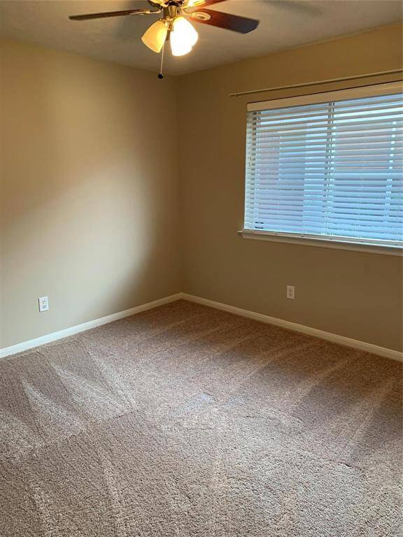 This 3rd bedroom features neutral walls, a ceiling fan with lights, and a large window with blinds. The carpeted floor adds warmth, making it ideal for a cozy bedroom or office space.