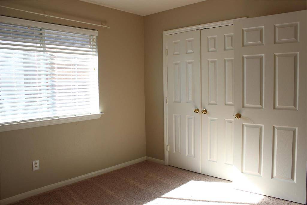 This photo shows a bright, neutral-colored room with a window featuring blinds, carpeted flooring, and a double-door closet. Perfect for a bedroom or home office.