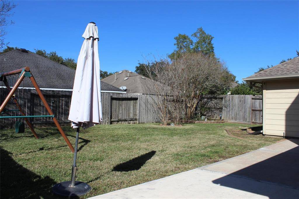 Spacious backyard with well-maintained grass, a wooden swing set, and a patio area. Fenced for privacy, perfect for outdoor activities.