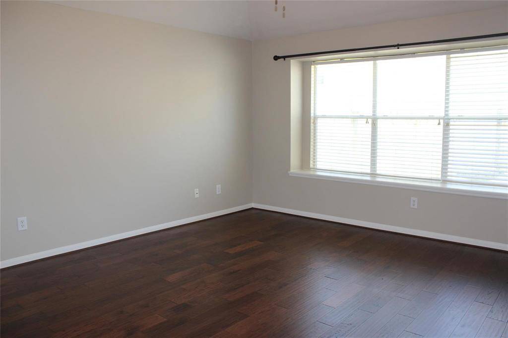 Master bedroom features a large window allowing natural light, neutral wall colors, and dark wood flooring, providing a bright and modern feel.