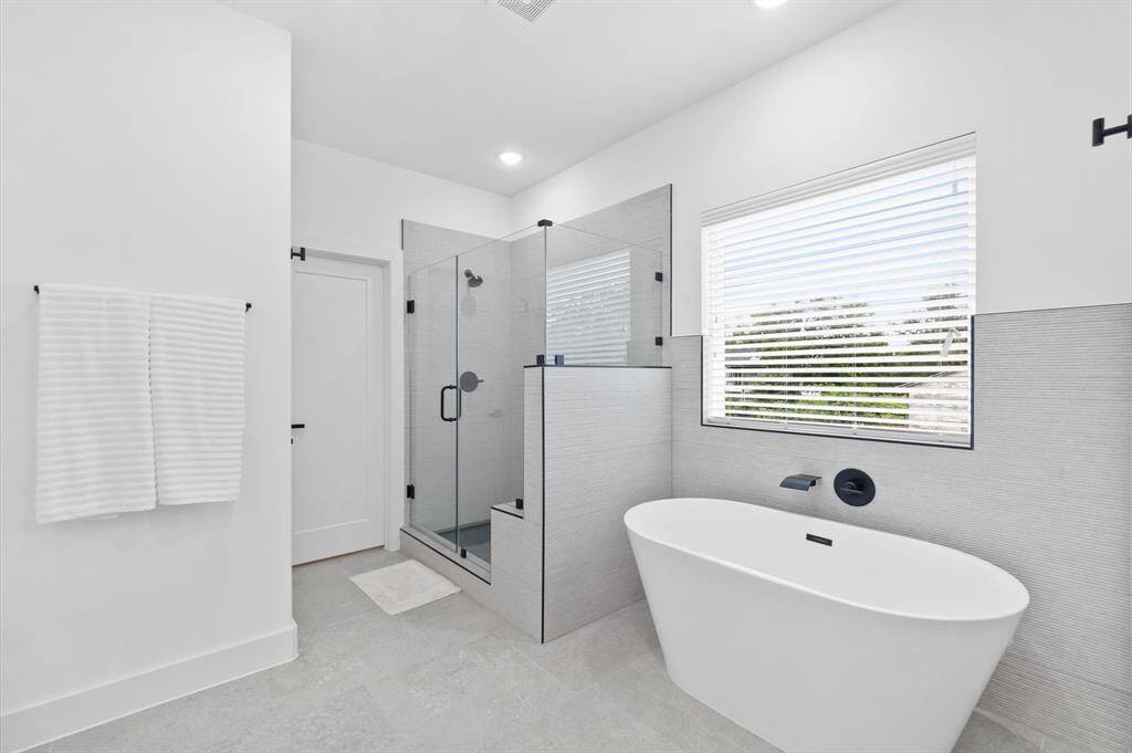 This elegant primary bathroom features a frameless glass shower, a luxurious oval soaking tub, and two spacious walk-in closets.