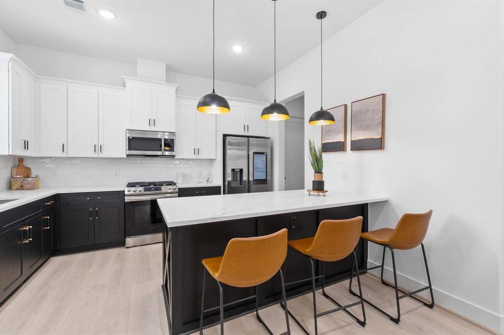 Modern kitchen with sleek black and white cabinetry featuring a breakfast bar, stainless steel appliances, and a peninsula with beverage center and pendant lighting.
