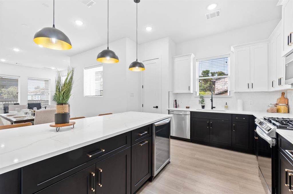 Modern kitchen with sleek black and white cabinetry featuring a breakfast bar, stainless steel appliances, and a peninsula with beverage center and pendant lighting.