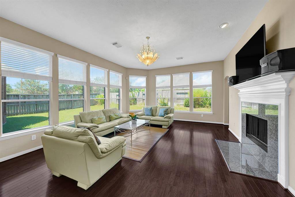 The living room boasts hard wood flooring, a beautiful chandelier, a gas-log fireplace, built-in shelving, and plenty of natural light from the windows.