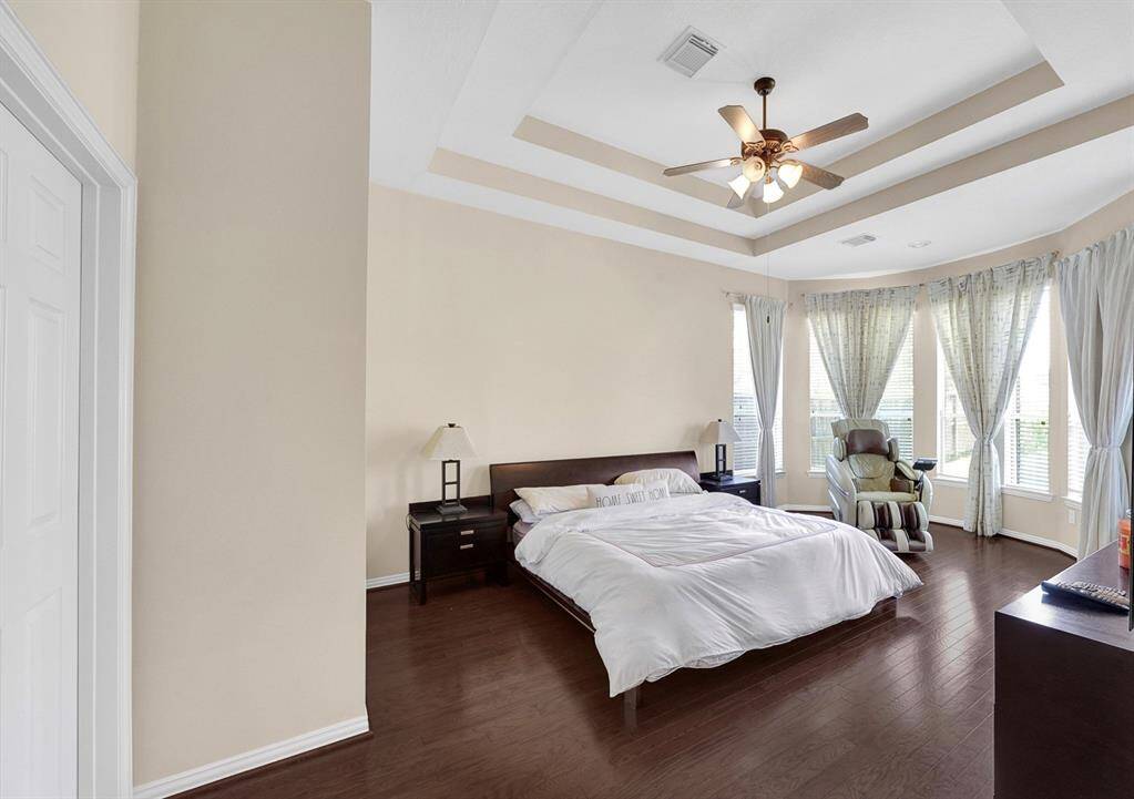 Primary suite with hardwood floors, trayed ceiling, and bonus space overlooking the backyard.