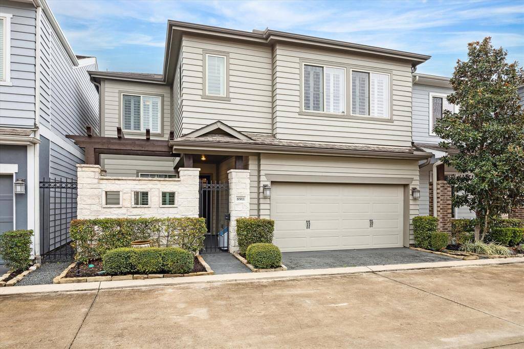 This modern two-story home features a sleek exterior with light gray siding, a two-car garage, and attractive landscaping. The property is accentuated by a stone entrance and a small courtyard, offering a welcoming and stylish curb appeal.